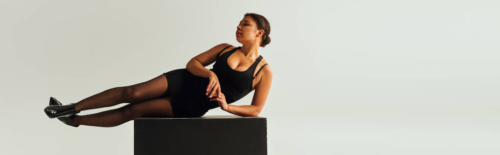 vonzó afro-amerikai női modell szexi öltözékben fekvő fekete kocka, divat koncepció, banner - Fotó, kép