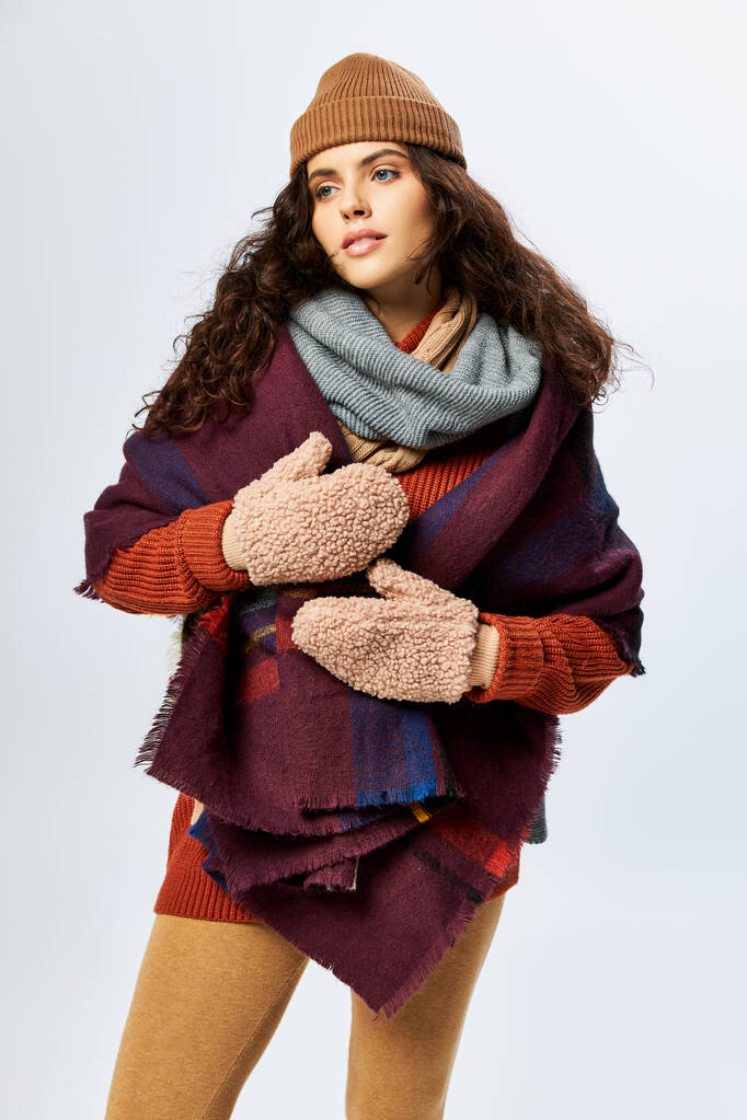 уютные слои, брюнетка женщина в слоистой одежде с теплым шарфом и варежки на сером фоне - Фото, изображение