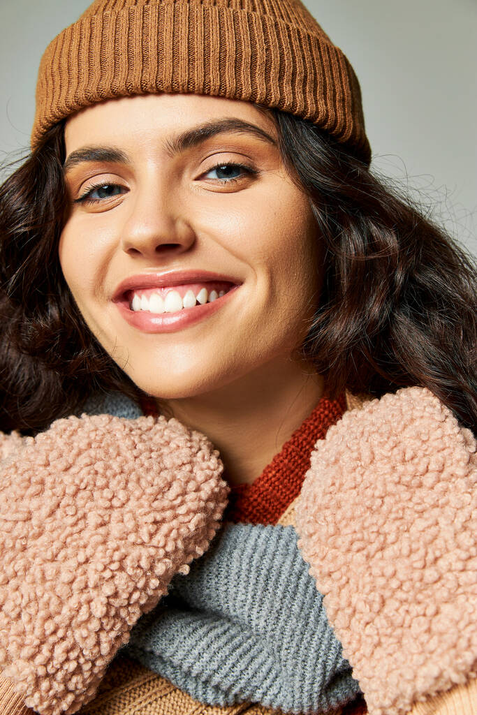 winter mode concept, gelukkige jonge vrouw in gebreide hoed en wanten glimlachen op grijze achtergrond - Foto, afbeelding