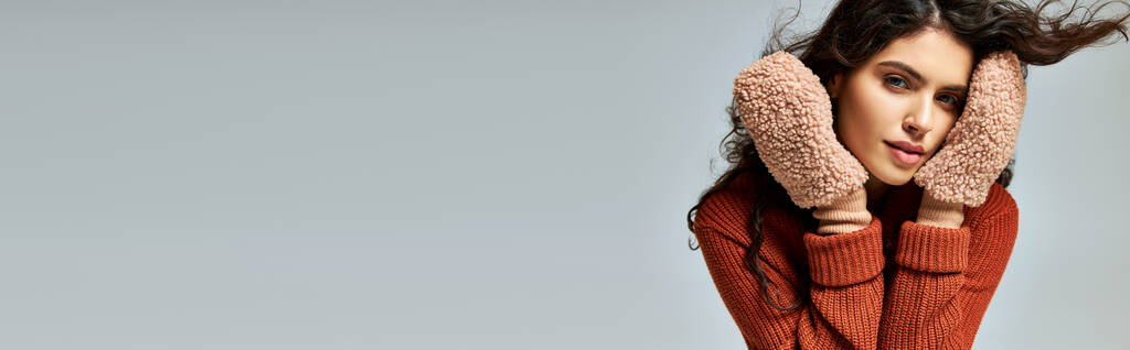 göndör barna nő terrakotta pulóver és puha kesztyű pózol szürke, téli divat banner - Fotó, kép