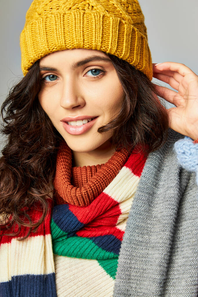 portrait of happy woman with curly hair in bobble hat and cozy sweater with stripped scarf - Photo, Image