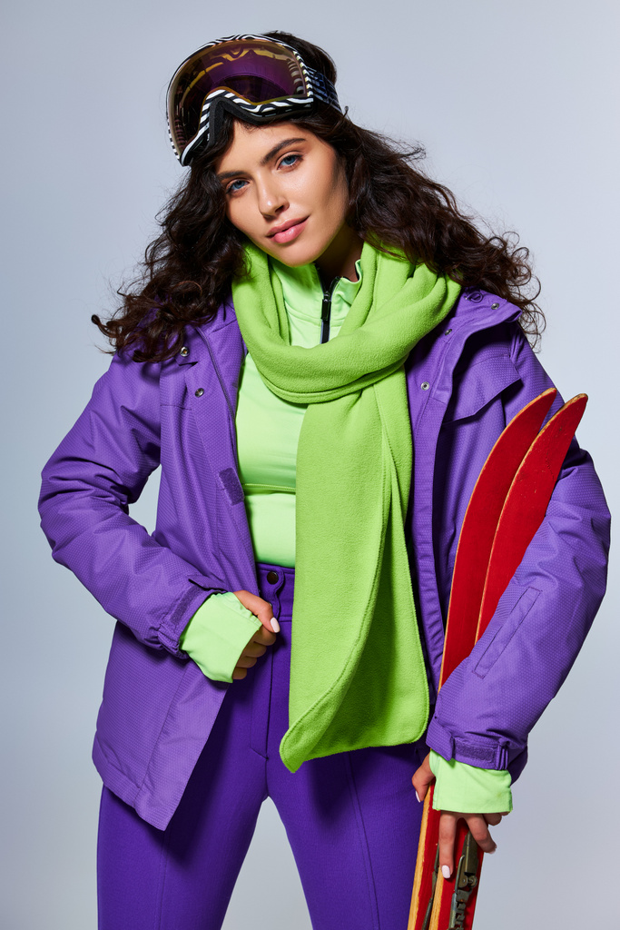 sport zimowy, atrakcyjna kobieta z kręconymi włosami pozowanie w aktywnym stroju z kurtką puffer i narty - Zdjęcie, obraz