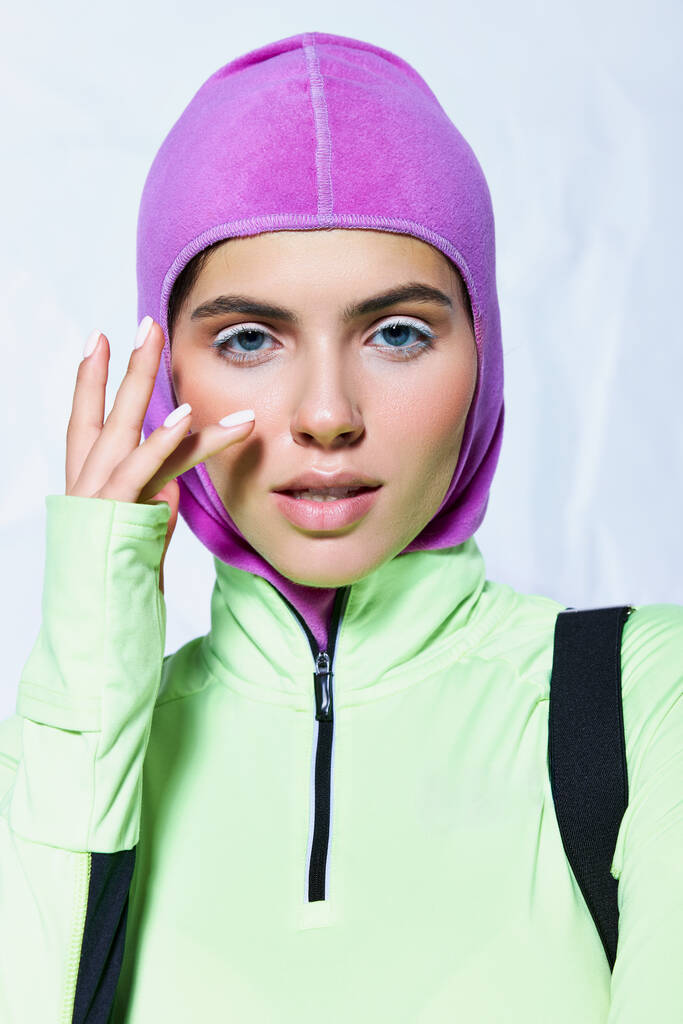 portrait of beautiful woman with blue eyes posing in ski mask and active wear on grey backdrop - Photo, Image