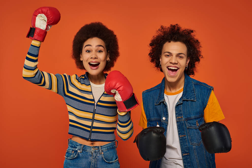 alegres hermanos afroamericanos en guantes de boxeo divirtiéndose juntos sobre fondo naranja, familia - Foto, imagen