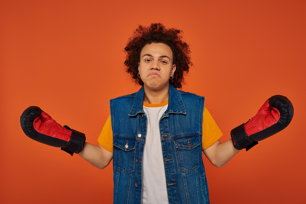 confused sporty african american male model posing lively in boxing gloves on orange background - Photo, Image