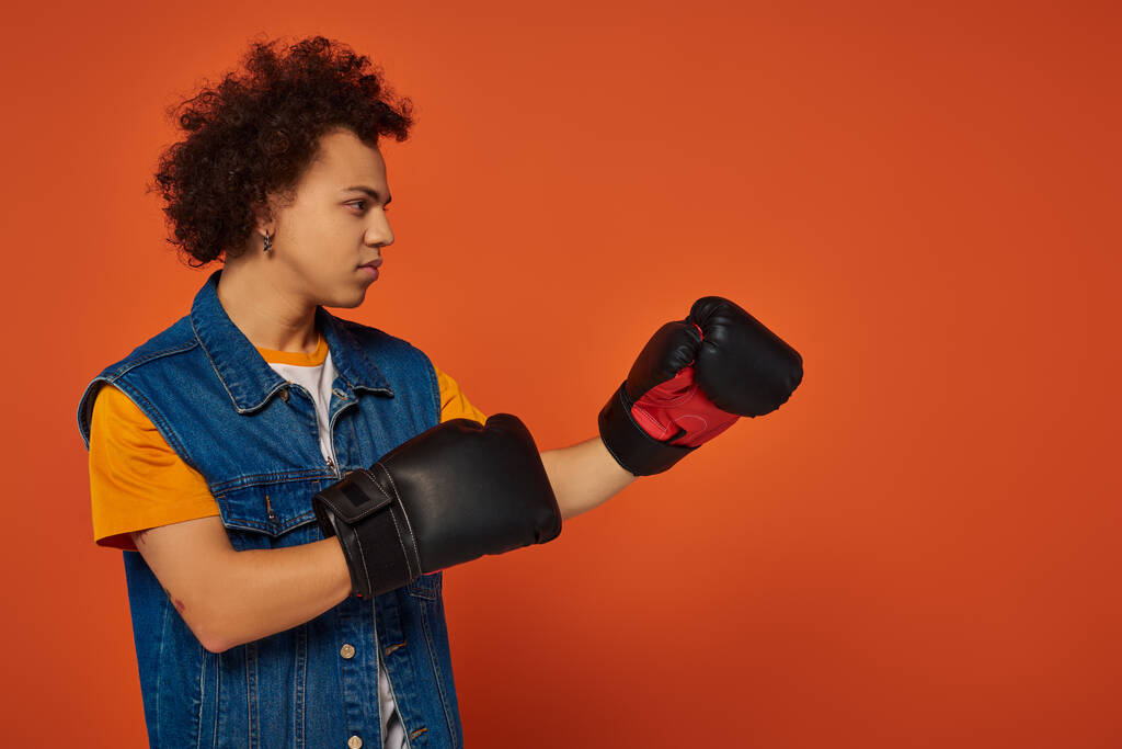 オレンジ色の背景にボクシング手袋に活発にポーズするアスリートアフリカ系アメリカ人男性 - 写真・画像