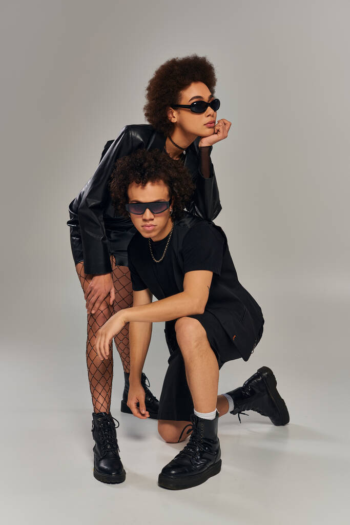 stylové africké americké sourozence v módní černé oblečení se slunečními brýlemi pózovat na šedém pozadí - Fotografie, Obrázek