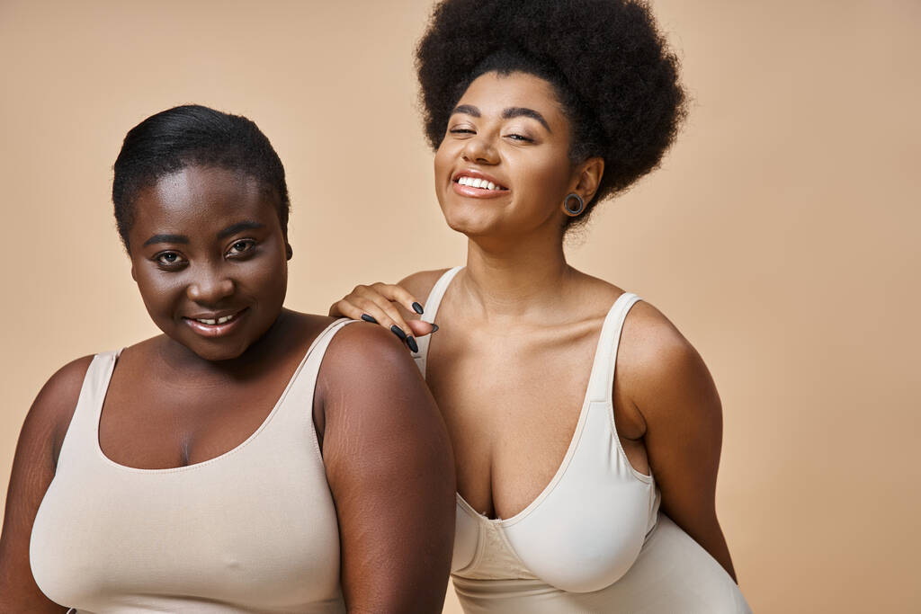 gelukkig plus size Afrikaans amerikaanse vrouwen in lingerie glimlachen op camera op beige, lichaam positiviteit - Foto, afbeelding