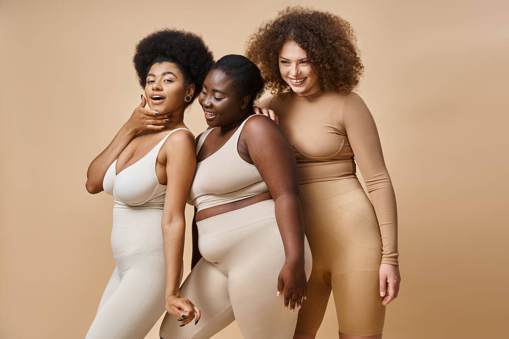 gioiosa multietnico plus size donne in biancheria intima in posa su sfondo beige, fiducia in se stessi e il fascino - Foto, immagini