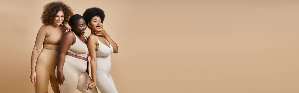 vreugdevolle multi-etnische plus size vrouwen in ondergoed poseren op beige achtergrond, zelfvertrouwen, banner - Foto, afbeelding