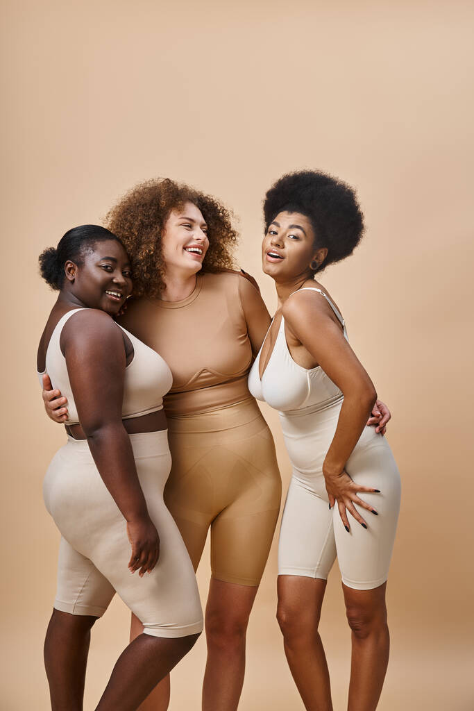 šťastný multietnické tělo pozitivní ženy ve spodním prádle objímající na béžové, přírodní křivky krásy - Fotografie, Obrázek