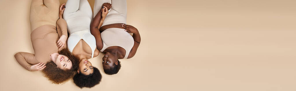 top view of happy plus size kobieta w bieliźnie leżącej na beżu, body positive beauty, banner - Zdjęcie, obraz