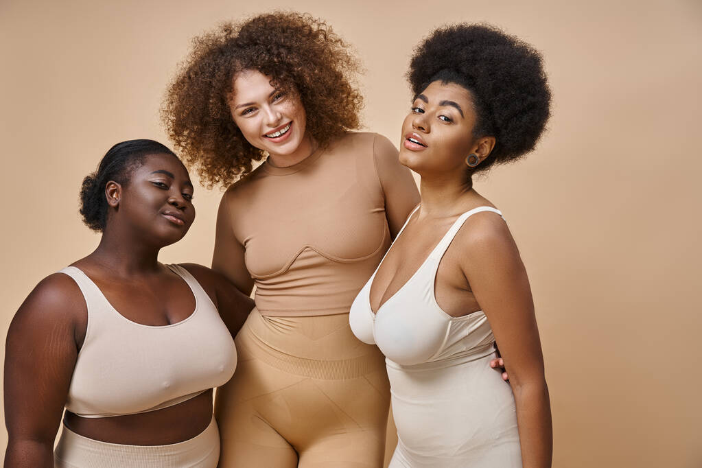 happy multiethnic plus size girlfriends in lingerie posing on beige backdrop, body positive beauty - Photo, Image