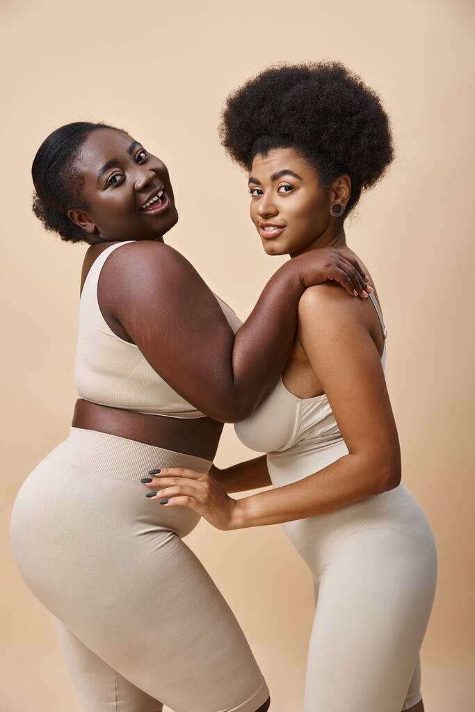 sensuale e sorridente plus size donne africane americane in posa in lingerie su beige, bellezza curvy - Foto, immagini