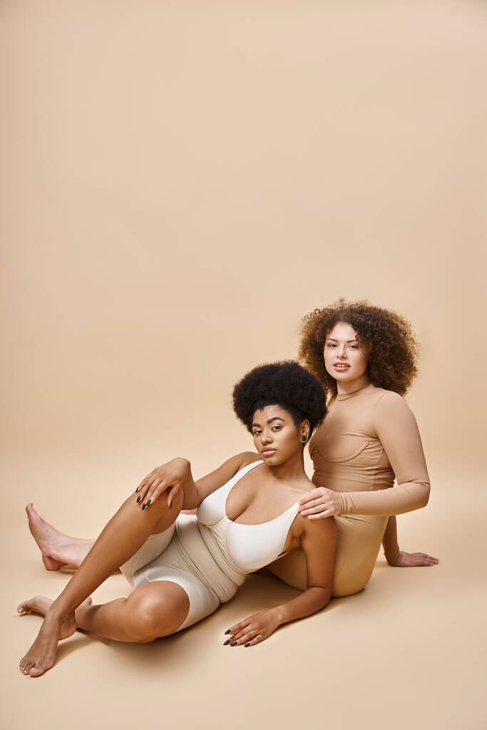 gai multiculturel plus la taille copines en lingerie assis sur fond beige, beauté naturelle - Photo, image