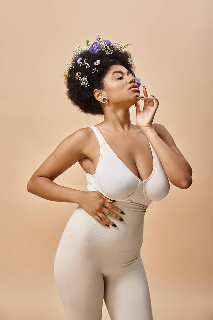 aistillinen afrikkalainen amerikkalainen nainen värikkäitä kukkia hiukset poseeraa alusvaatteita beige taustalla - Valokuva, kuva