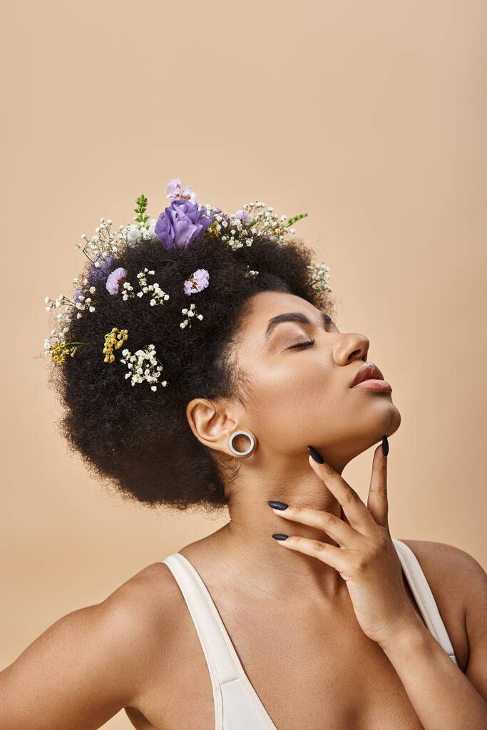 zmysłowa Afroamerykanka z kolorowymi kwiatami we włosach pozowanie z zamkniętymi oczami na beżu - Zdjęcie, obraz