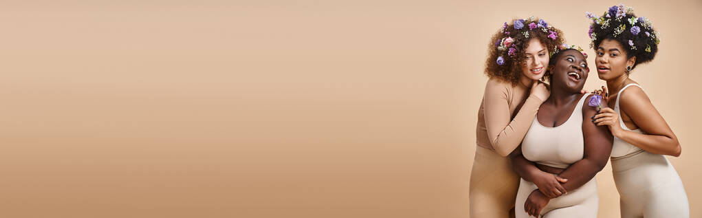 счастливые многорасовые плюс размер женщин в нижнем белье с красочными цветами в волосах на бежевый, баннер - Фото, изображение