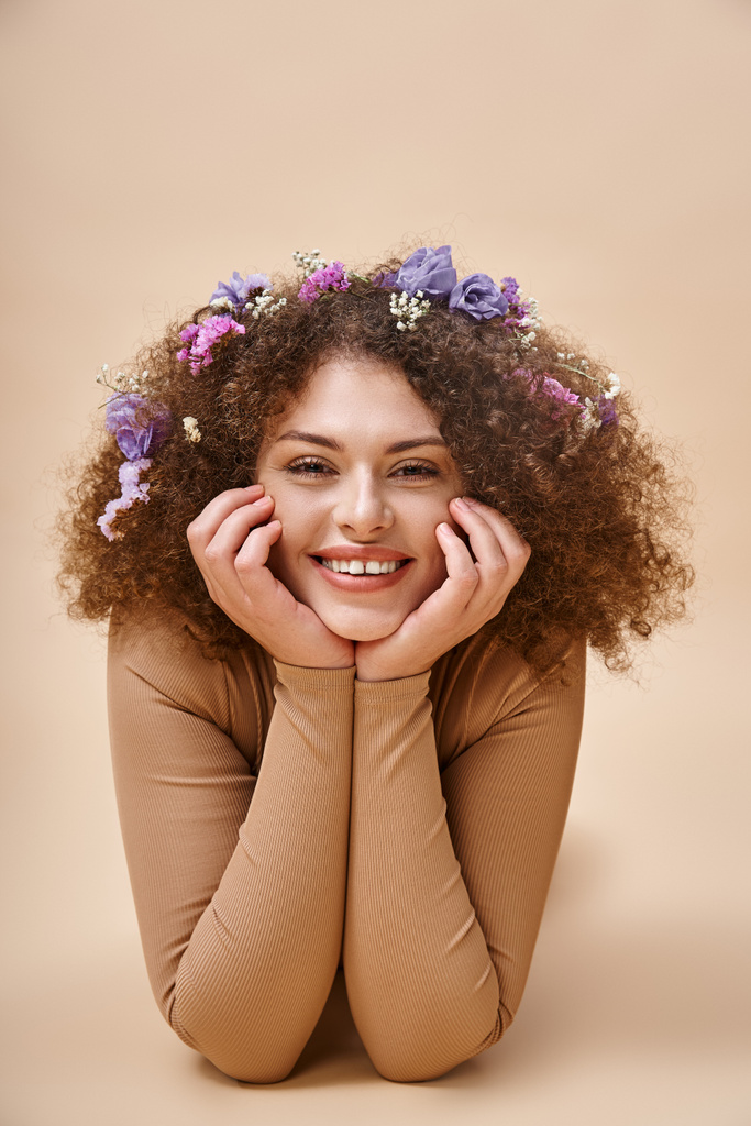 πορτρέτο της όμορφης και χαρούμενης γυναίκας με πολύχρωμα λουλούδια σε κυματιστά μαλλιά σε μπεζ, φυσική ομορφιά - Φωτογραφία, εικόνα