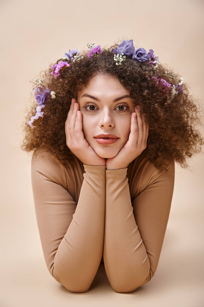 portrait of pretty and expressive woman with colorful flowers in wavy hair on beige, natural beauty - Photo, Image