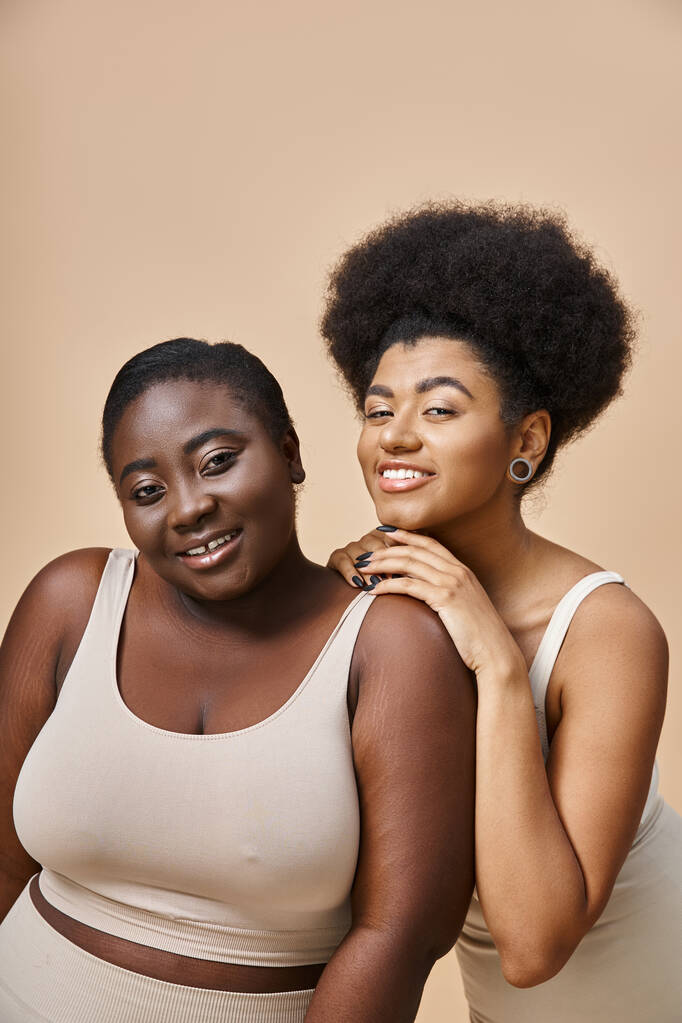 cheerful african american female models in underwear looking at camera on beige, plus size beauty - Photo, Image