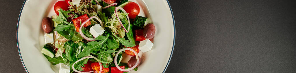 Foto von oben von Teller mit frisch zubereitetem köstlichen griechischen Salat auf grauem Hintergrund, Banner - Foto, Bild