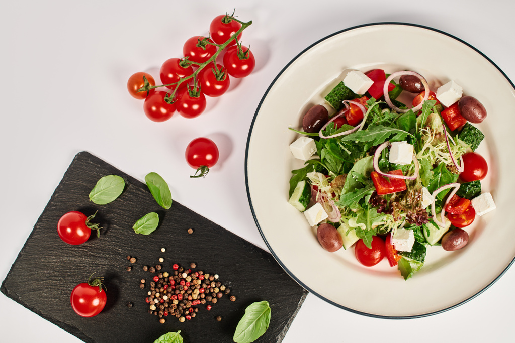 foto vista superior da placa com salada grega tradicional perto de tomates cereja e folhas de manjericão - Foto, Imagem
