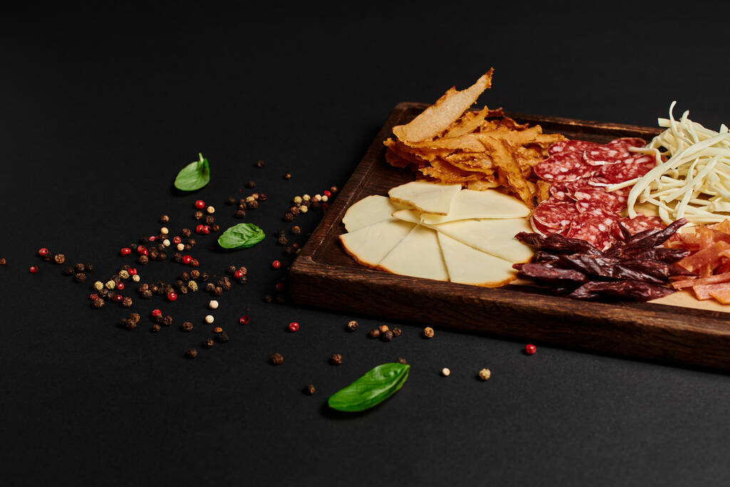charcuterie board o comida de fiesta con selección de quesos gourmet, carne seca y rebanadas de salami en negro - Foto, Imagen