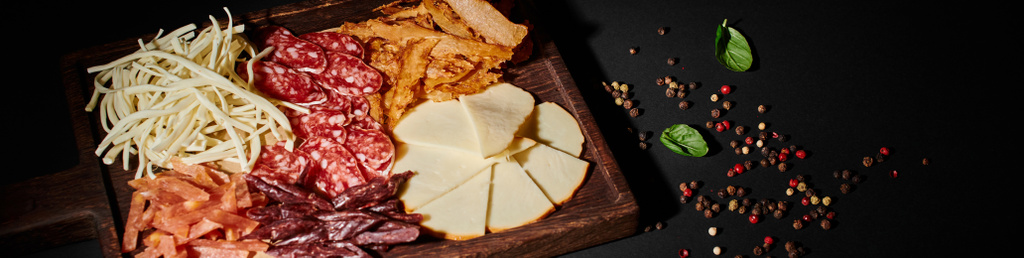 баннер из фартука с изысканным выбором сыра, сушеной говядины и ломтиками салями на черном - Фото, изображение