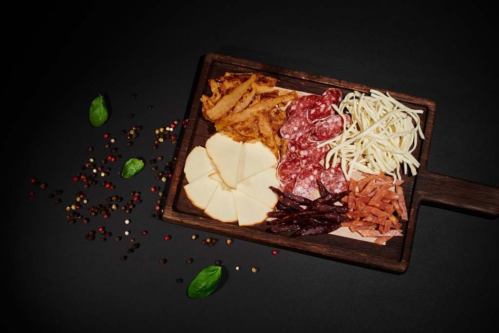 vista superior del tablero de comida de fiesta con selección de queso gourmet, carne seca y rebanadas de salami en negro - Foto, Imagen