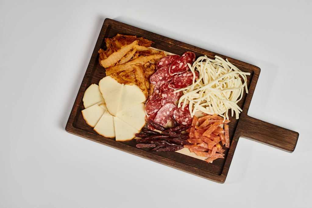 tabla de charcutería con plato de queso gourmet, carne seca y rebanadas de salami sobre fondo gris - Foto, Imagen