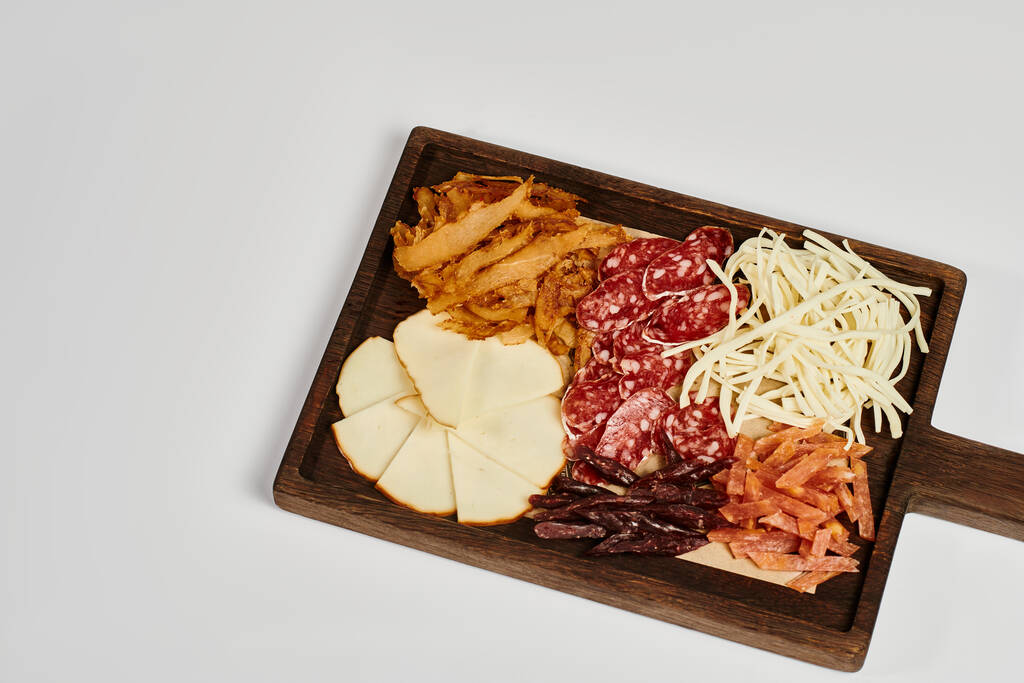доска для вечеринок с блюдом из сыра для гурманов, сушеной говядиной и ломтиками салями на сером фоне - Фото, изображение
