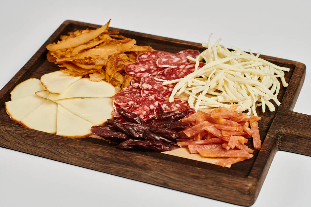 tabla de embutidos con sabrosa bandeja de queso, carne seca y rebanadas de salami sobre fondo gris - Foto, imagen