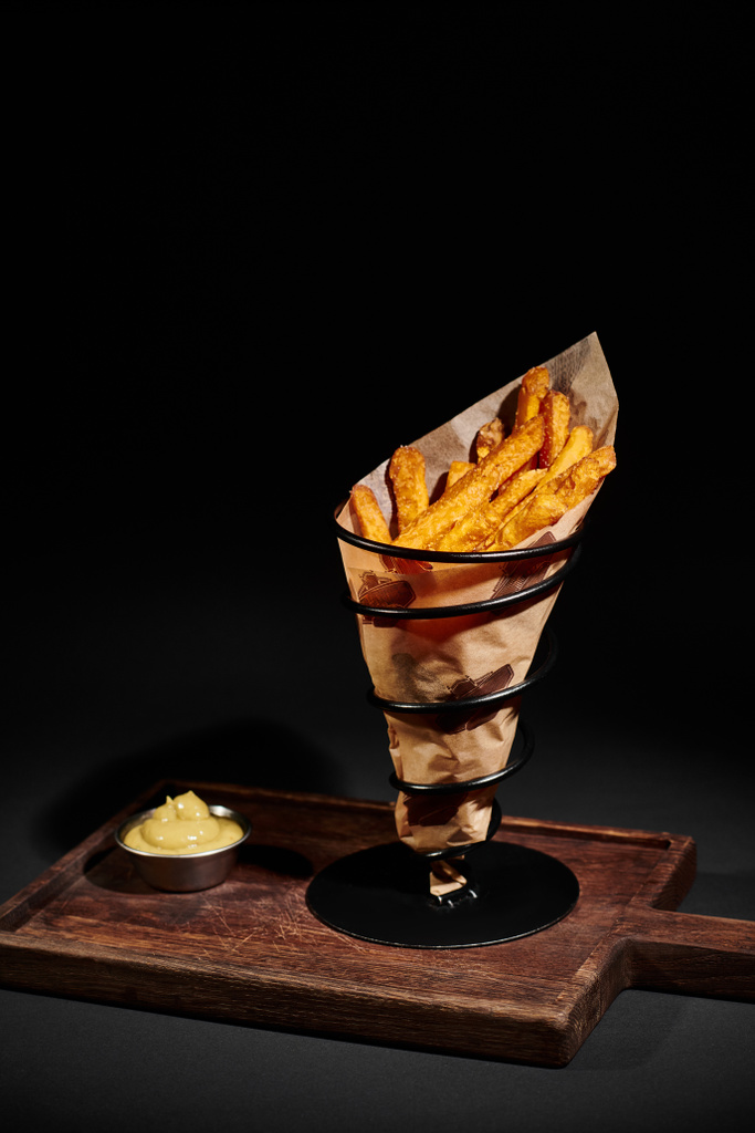 deliciosas batatas fritas crocantes dentro do cone de papel perto de molho de mergulho na placa de corte de madeira - Foto, Imagem