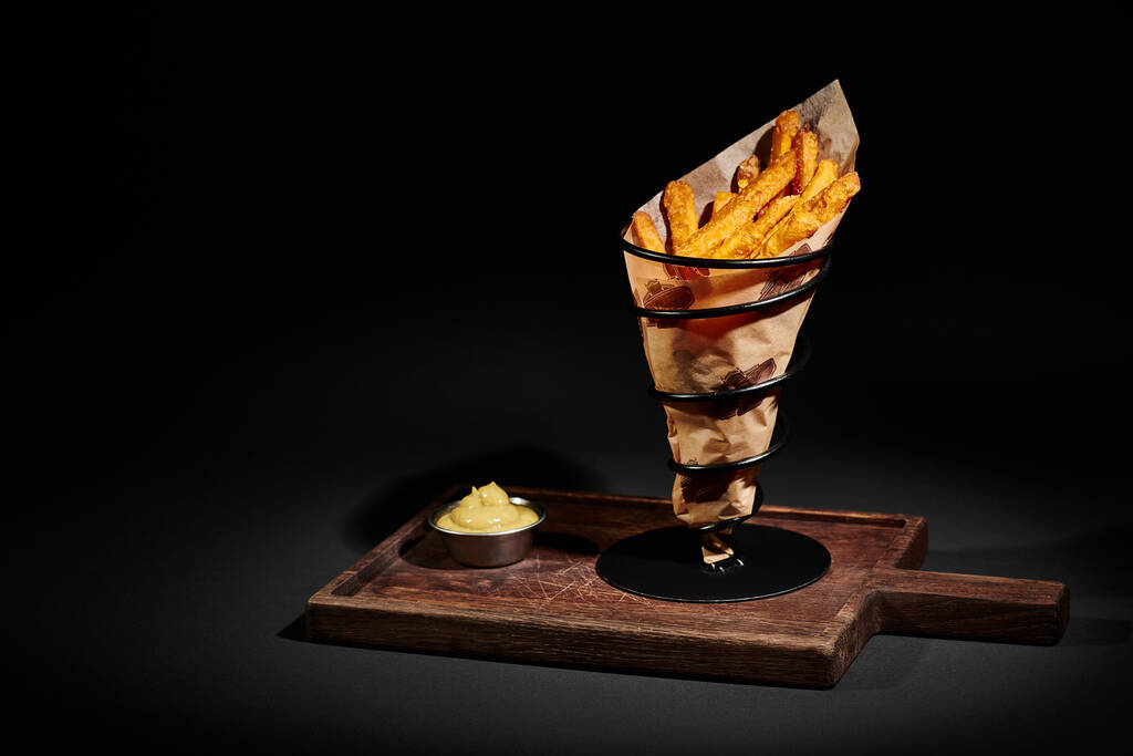 deliciosas y crujientes papas fritas dentro del cono de papel cerca de la salsa de inmersión en la tabla de cortar de madera - Foto, imagen