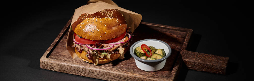 leckere Burger mit Sesambrötchen, Rindfleisch und Essiggurken als Beilage auf Holztablett auf schwarz, Banner - Foto, Bild