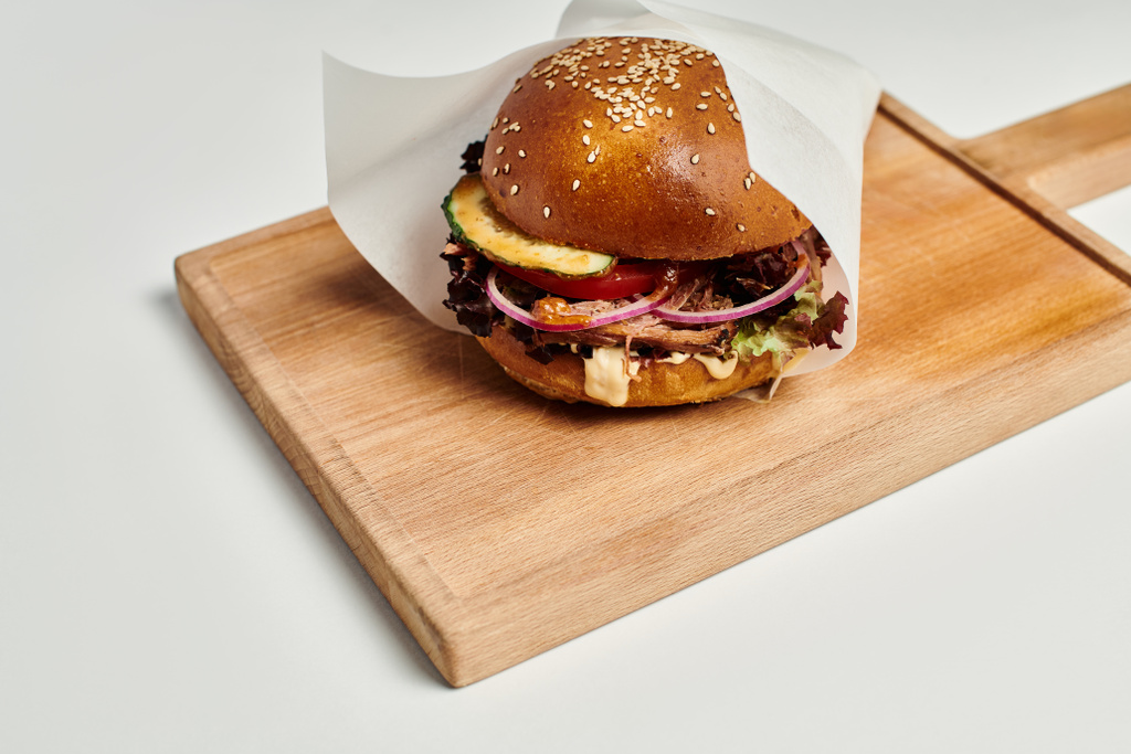 hamburguesa jugosa con carne a la parrilla, cebolla roja, queso derretir y pan de sésamo en la tabla de cortar de madera - Foto, Imagen
