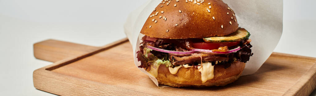 гамбургер с жареной говядиной, красным луком, плавленым сыром и булочкой кунжута на деревянной доске, баннер - Фото, изображение