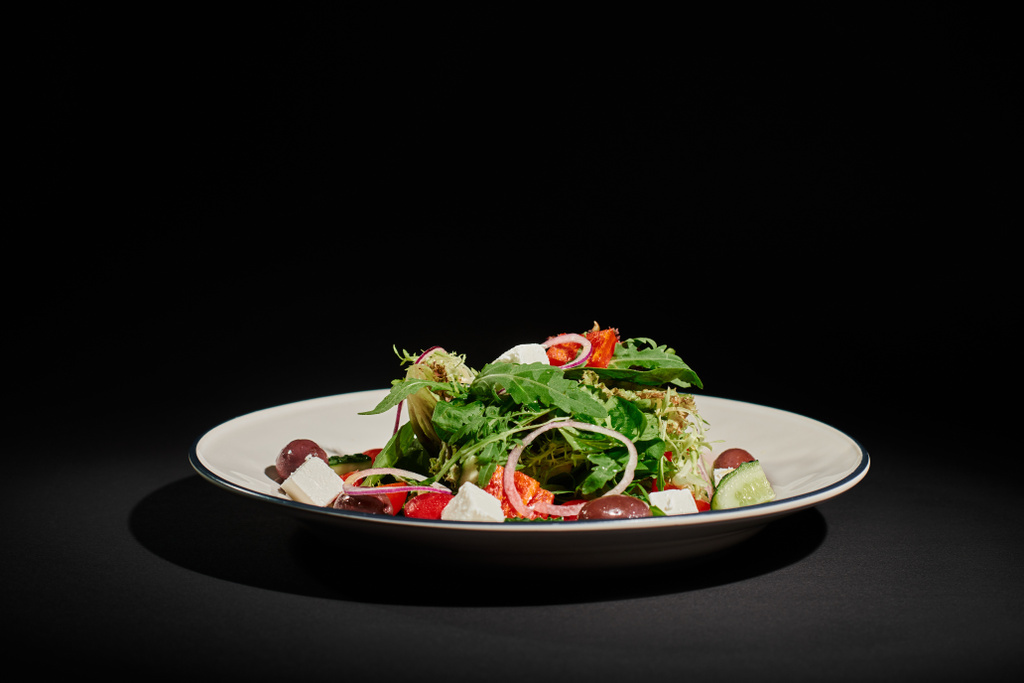 zdrowe odżywianie, pyszna sałatka grecka z serem feta, czerwona cebula, liście rukoli na czarnym tle - Zdjęcie, obraz