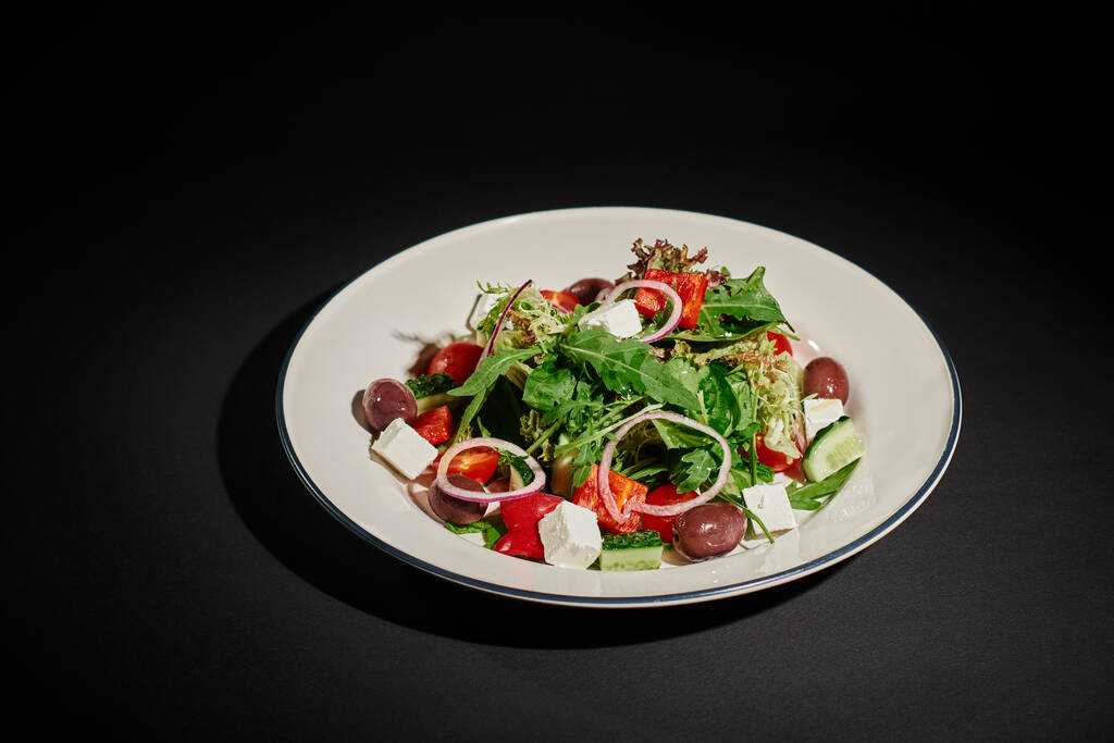 repas léger, délicieuse salade grecque au fromage feta, oignon rouge, feuilles de roquette sur fond noir - Photo, image