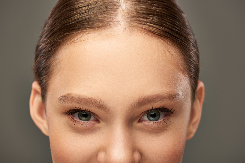 обрізаний вид на молоду жінку з блакитними очима і ідеальною шкірою, дивлячись на камеру на сірому фоні - Фото, зображення