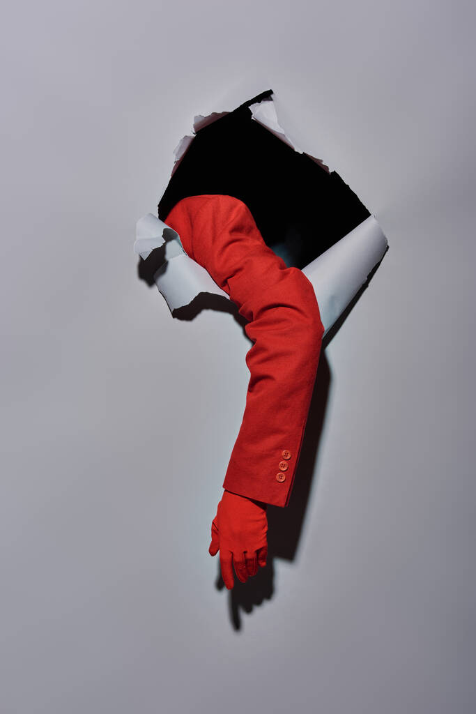 rajattu näkymä nainen punainen hiha ja käsine murtaa vaikka reikä harmaa tausta, käsitteellinen - Valokuva, kuva
