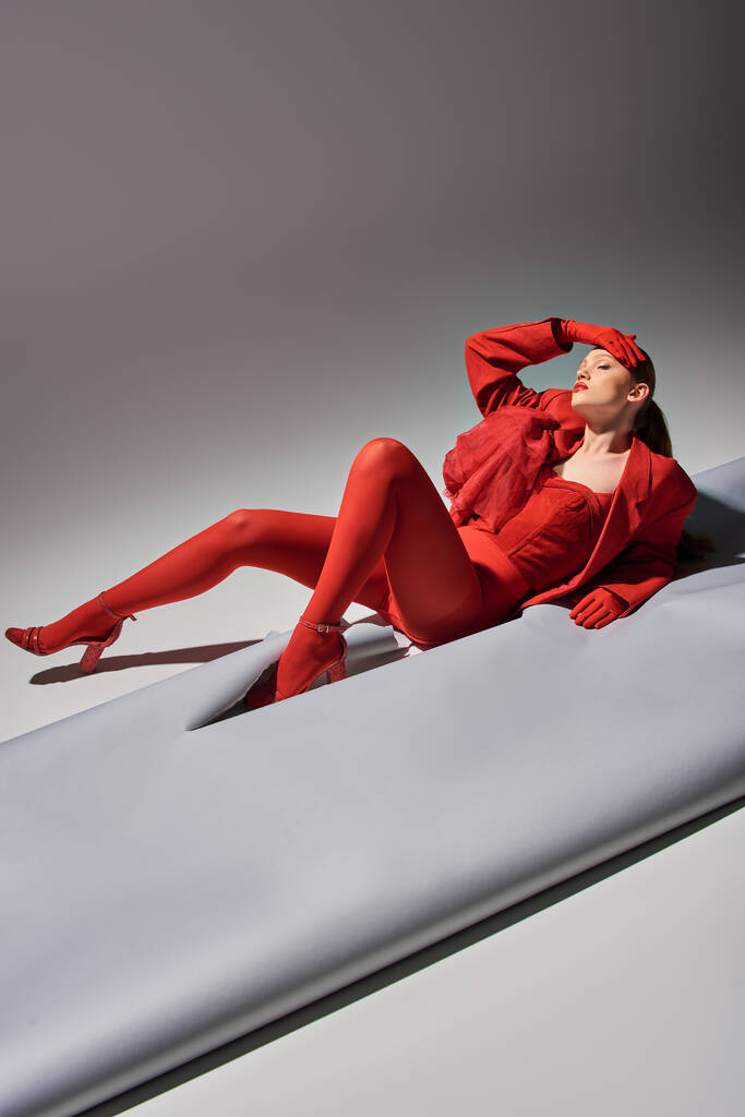 teljes hossza csinos fiatal modell piros ruhában kesztyűvel és blézer pózol szürke háttér - Fotó, kép
