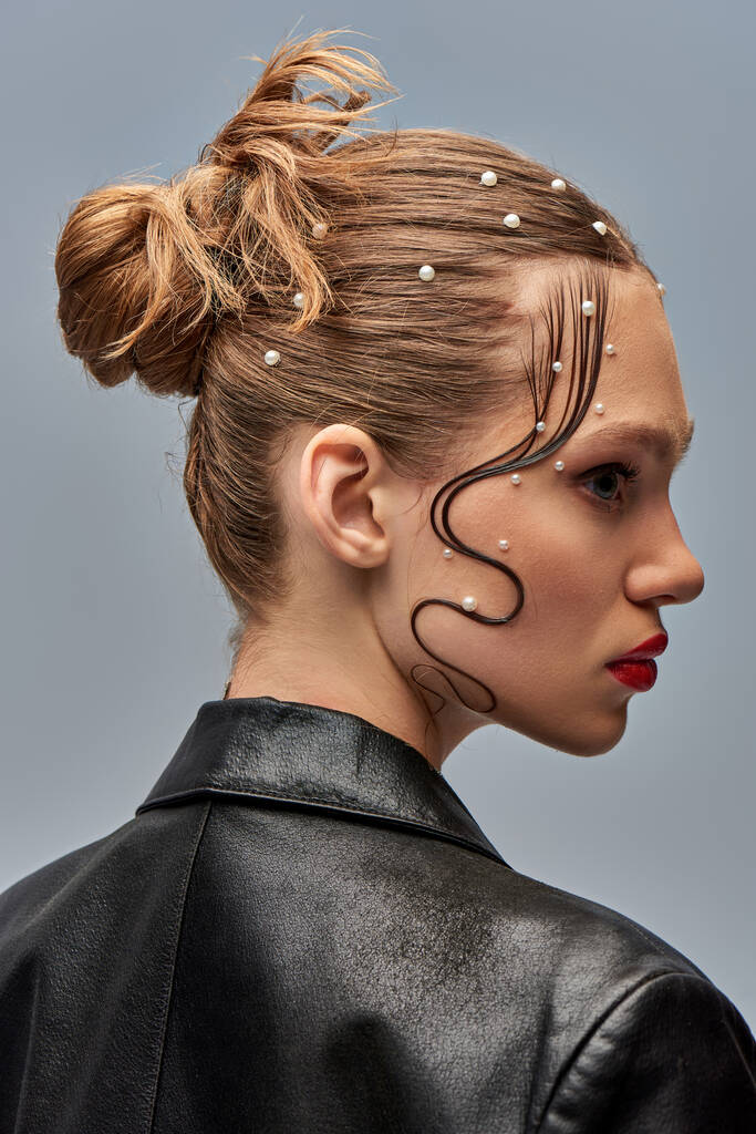 профиль симпатичной молодой модели с модными жемчужными булавками в волосах и красными губами, позирующими на сером фоне - Фото, изображение