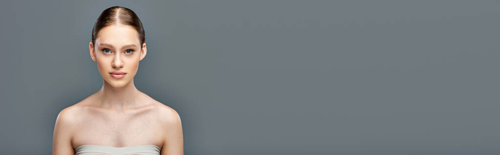 kein Make-up-Banner, schöne junge Frau mit nackten Schultern, die in die Kamera auf grauem Hintergrund blickt - Foto, Bild