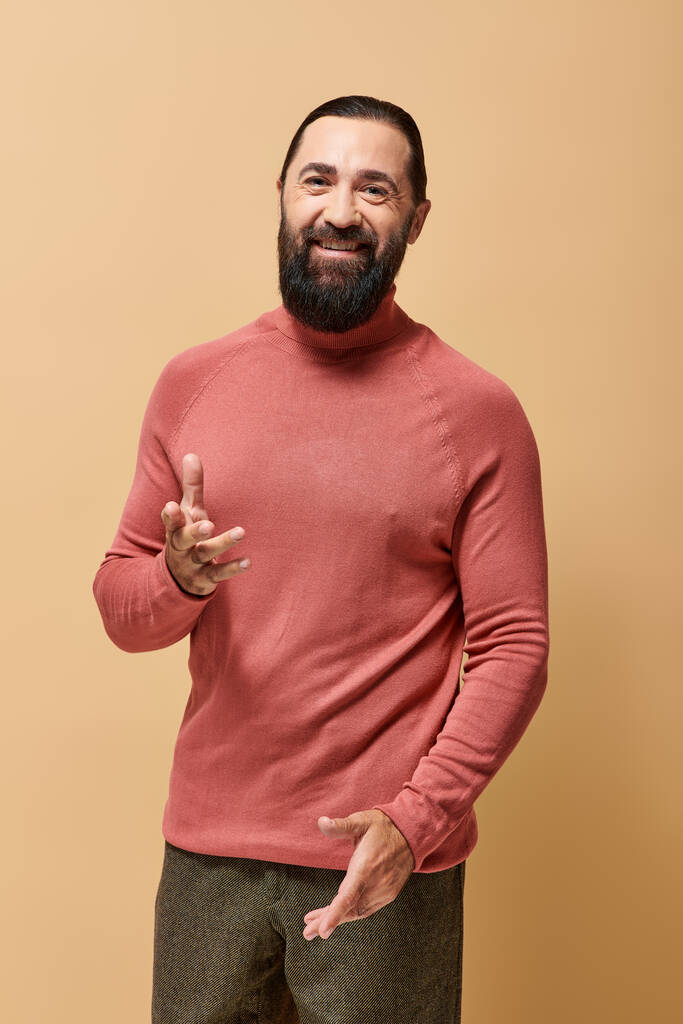happy man with beard in pink turtleneck jumper smiling cheerfully on beige backdrop, joy - Photo, Image