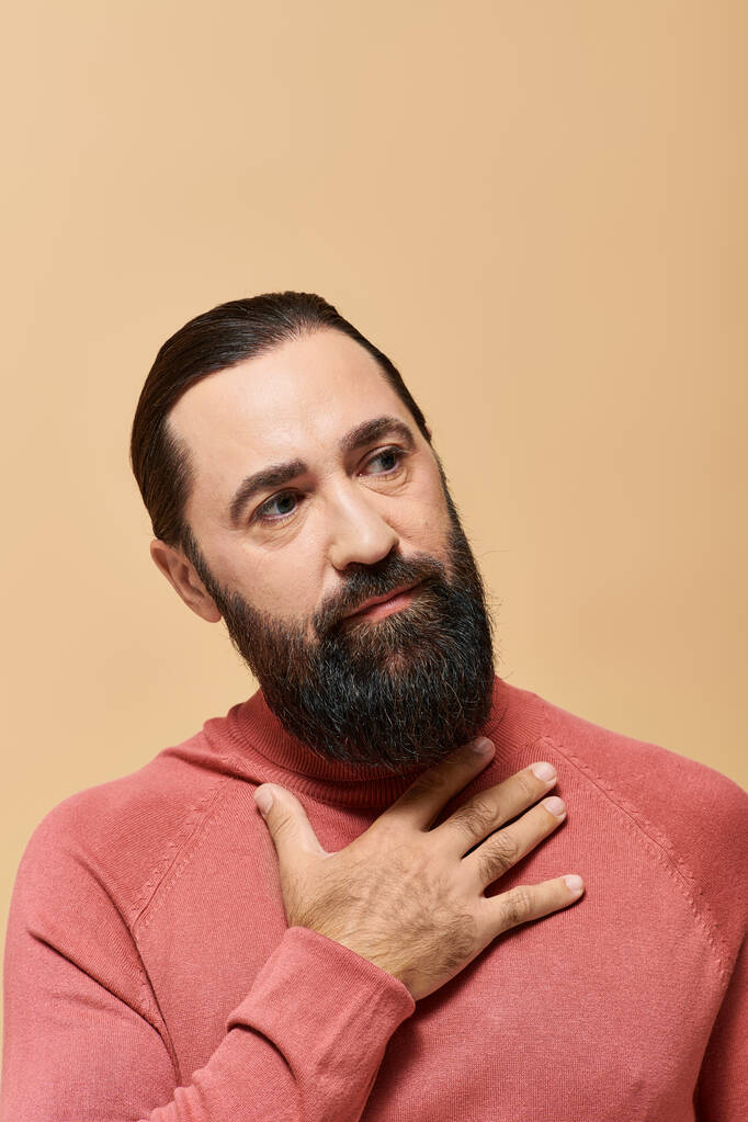 portret, poważny i przystojny mężczyzna z brodą pozujący w swetrze na beżowym tle - Zdjęcie, obraz