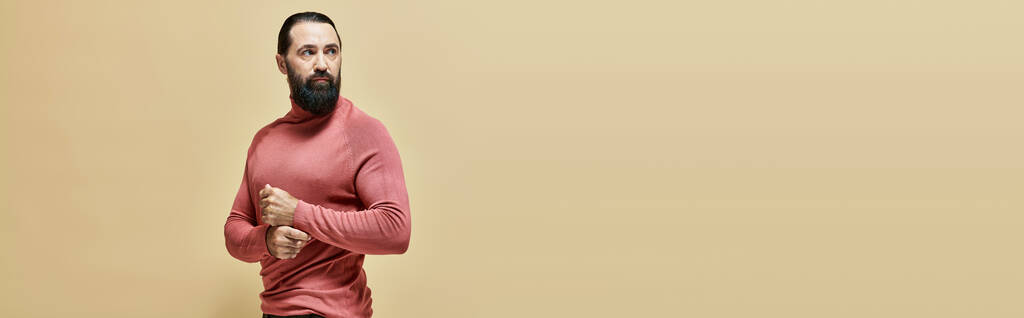 vážně dobře vypadající muž s vousy pózující v růžovém roláku jumper na béžové pozadí, banner - Fotografie, Obrázek