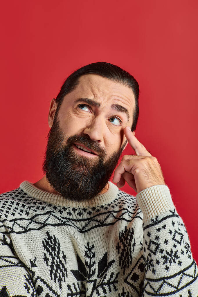 bearded man in Christmas sweater with ornament thinking and pointing at head on red background - Photo, Image