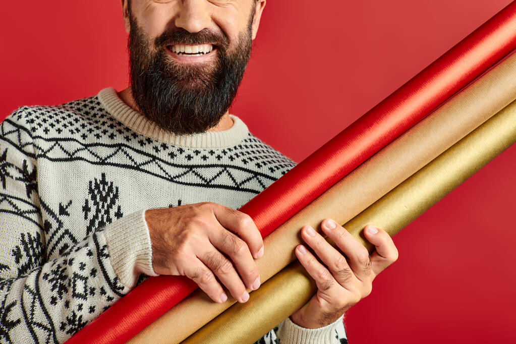 rajattu onnellinen parrakas mies talvella villapaita tilalla lahjapaperia punaisella taustalla, Hyvää joulua - Valokuva, kuva